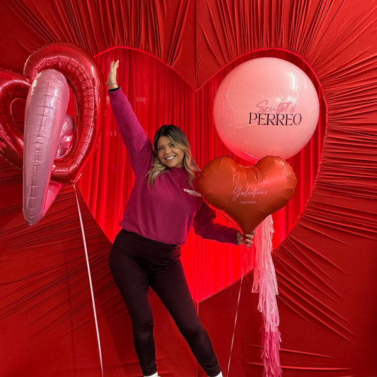 Person posing with heart-shaped balloons in front of a red backdrop